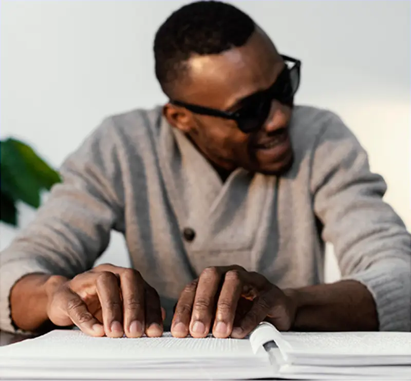 Imagem de um rapaz com óculos fazendo a leitura em braile.