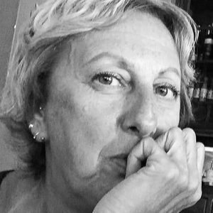 Arlete tem pele em tom claro, cabelos loiros, curtos e lisos e olhos verdes. Usa brincos. A foto está em preto e branco e ela está com o rosto apoiado na mão, com expressão séria.